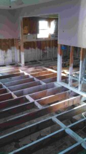 Interior of a Jersey Shore home showing flood damage remediation — exposed floor joists, gutted walls, and waterline staining on wall framing after storm flooding